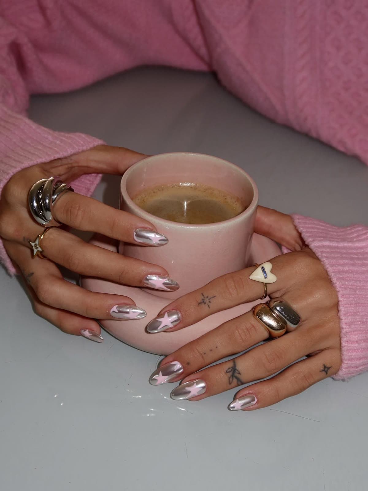 Two hands with chrome and pink star press-on nails holding a pink cup
